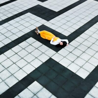 Woman in Yellow Pants Lying on Concrete Tiled Floor